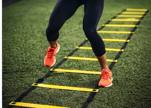 Person using a yellow agility ladder on a grassy field